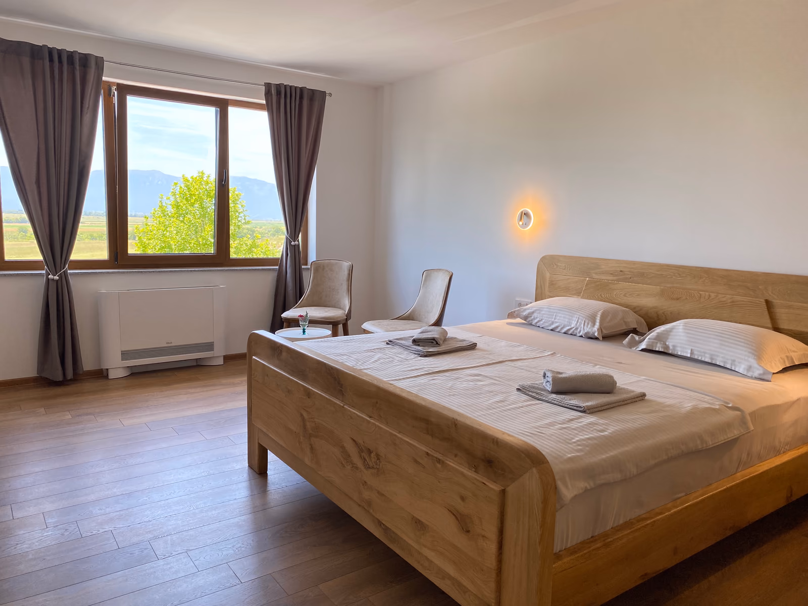 Zimmer im Motel Vujeva mit Doppelbett, zwei Sesseln und einem Fenster mit Blick auf Felder und Berge